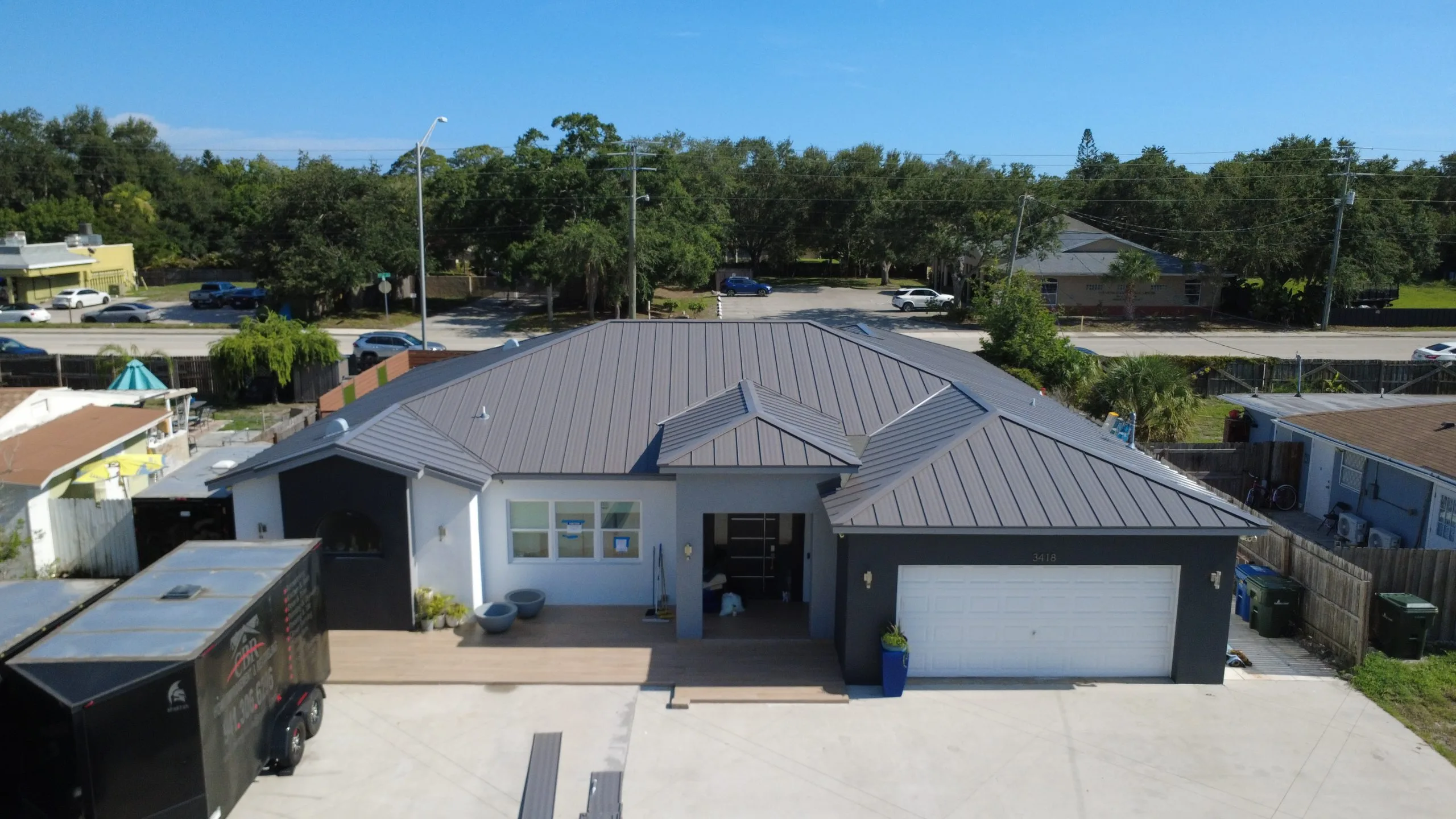 Completed grey standing seam metal roof replacement on a residential home in Sarasota, FL with a Barrier Builders contractor trailer in the driveway.